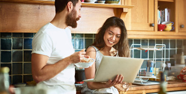 Couple standing in kitchen looking at laptop screen