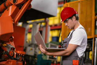 Worker wearing hard hat in warehouse, using laptop