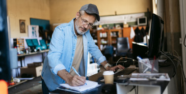 Entrepreneur Writing Notes And Using Computer In His Workshop