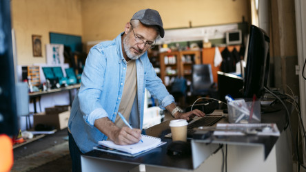Entrepreneur Writing Notes And Using Computer In His Workshop