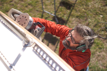 Man on a ladder sanding the outside of a house