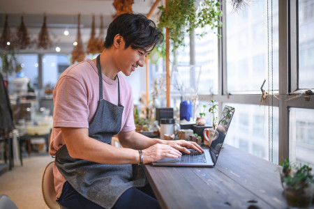 Man sitting at a work bench typing on his laptop.