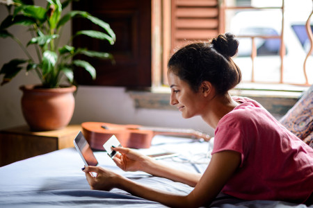 Woman on her bed with credit card in one hand and her tablet in the other hand