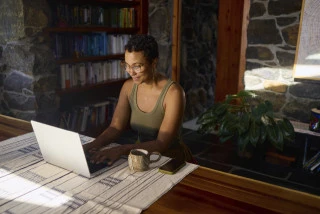 Female Working From Home On Laptop In Rustic House