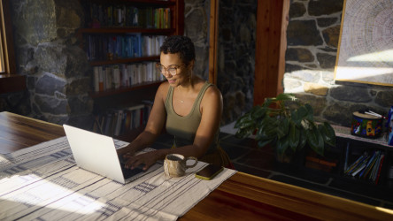Female Working From Home On Laptop In Rustic House