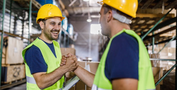 Two men in hard hats and hi viz vests shake hands.