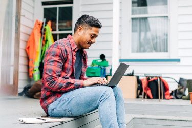 A man sitting on his deck, looking at his laptop