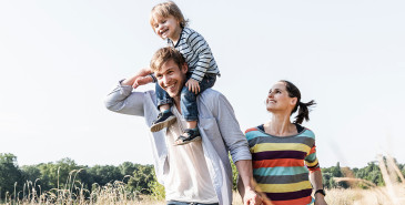 Cheerful family walking, with a child on the father’s shoulders, representing security.