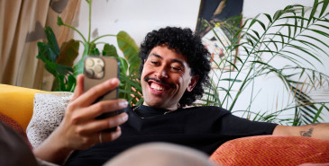 Young man sits on couch and smiles at his phone