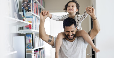A child sitting on the father’s shoulder smiling and representing security.