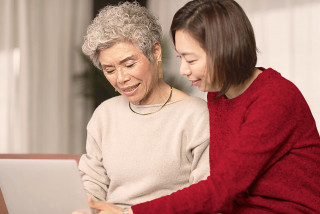 Adult child teaching their elderly parent how to use a laptop