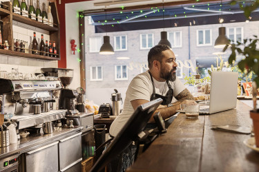 Cafe worker at counter browsing on laptop.
