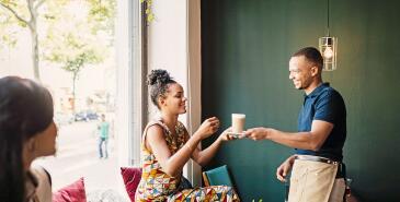 Person getting coffee from waiter in cafe.