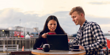 Couple drinking coffee and looking at laptop outdoors