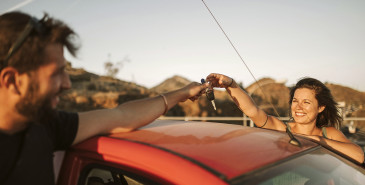 Couple handing over keys across car