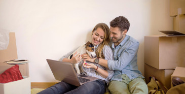 Couple sitting on floor of new home with dog and laptop on lap
