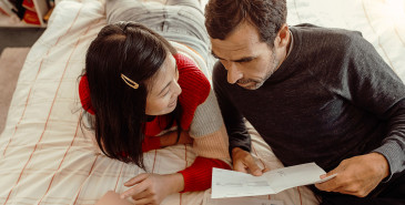 Couple sorting out bills on a bed