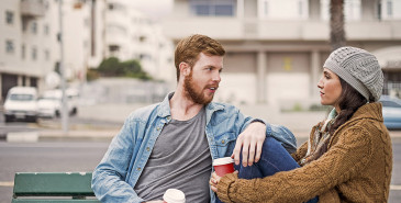 Friends on city bench talking while drinking take-away coffee