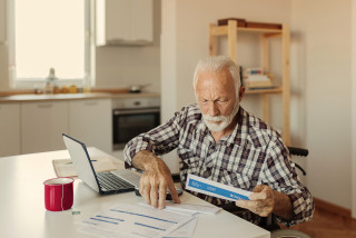 Elderly person in wheelchair at laptop sorting paper documents