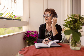 Elderly person looking out a window while on the phone