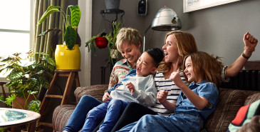 Family of four celebrating and laughing on sofa