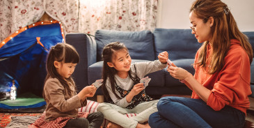 Parent and two children on floor playing cards