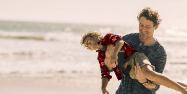 Parent holding child up on beach