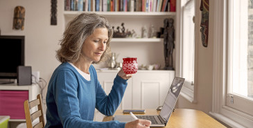 Person drinking hot drink writing in front of laptop