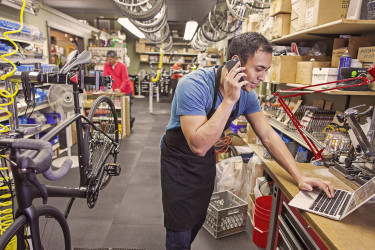 Person on phone and laptop at bike workshop