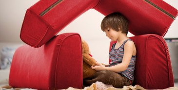 Child in pillow fort with teddy bear
