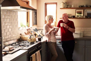 Senior couple standing in kitchen holding mugs
