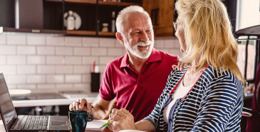 Senior couple sitting at the table, using laptop, looking at each other