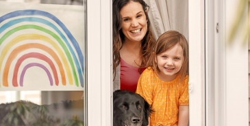 Smiling parent and child looking out of window with dog beside them.