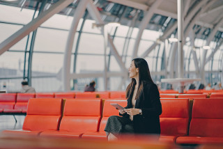 Smiling young person sitting in airport lounge and holding tablet