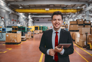 Smiling young business person holding digital tablet in factory
