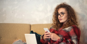 Young person sitting on couch using laptop and phone