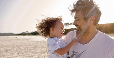 Parent hugging toddler on sunny beach