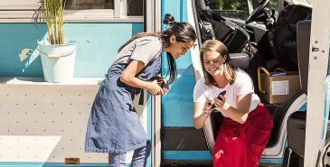 Two co-workers looking at a smartphone next to a blue van