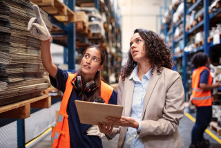 Warehouse worker pointing at the rack with a business person holding a clipboard.