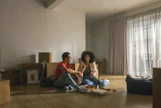 Couple sit on the floor of their new home eating pizza surrounded by boxes First