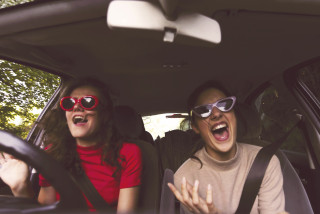 Two women wearing sunglasses in a car driving.