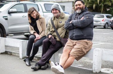 A woman and two men sitting on a low fence.