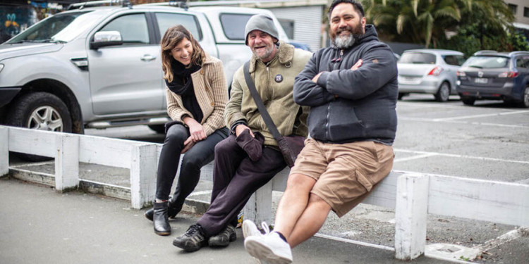 A woman and two men sitting on a low fence.