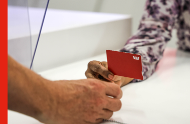 A man receives an eftpos card from a bank teller A man receives an eftpos card from a bank teller