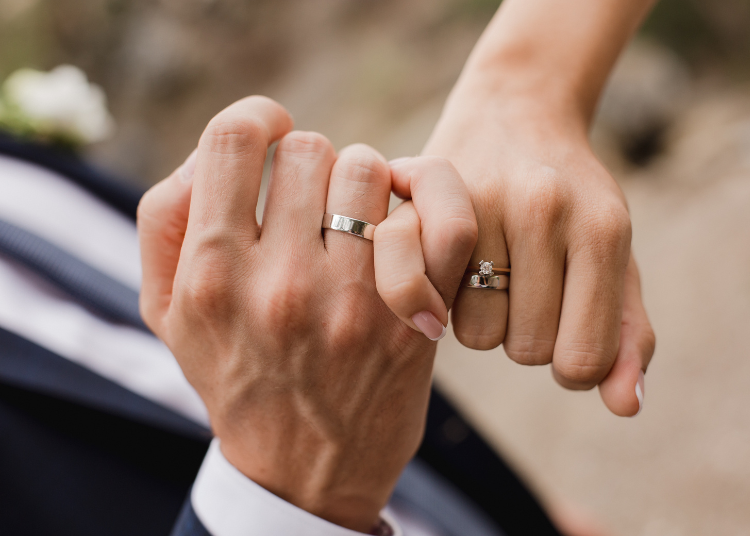 A couple interlock little fingers, showing their wedding rings