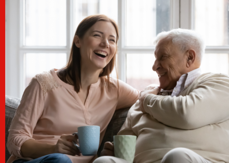 Untitled design 27 Young woman and old man sit on a couch enjoin a cup of tea.